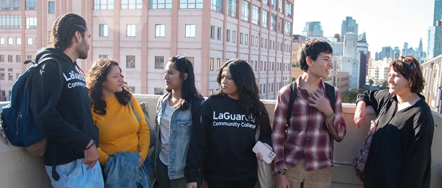 A group of 6 LaGuardia students talking at 7 train platform. They have LaGuardia College and Manhattan on the back